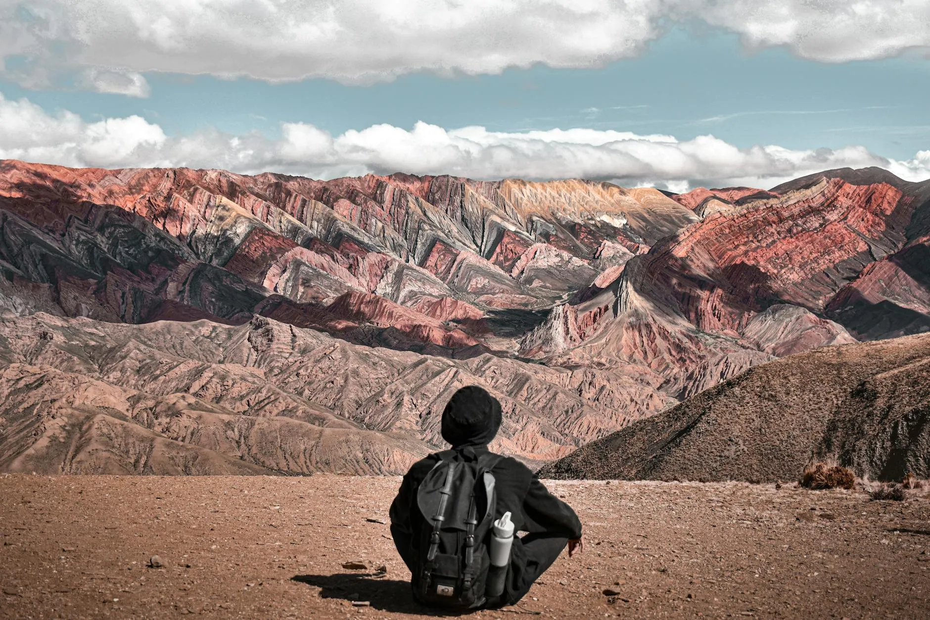A person sitting with a backpack enjoys the view of the colorful Serranía de Hornocal mountains in Jujuy, Argentina.