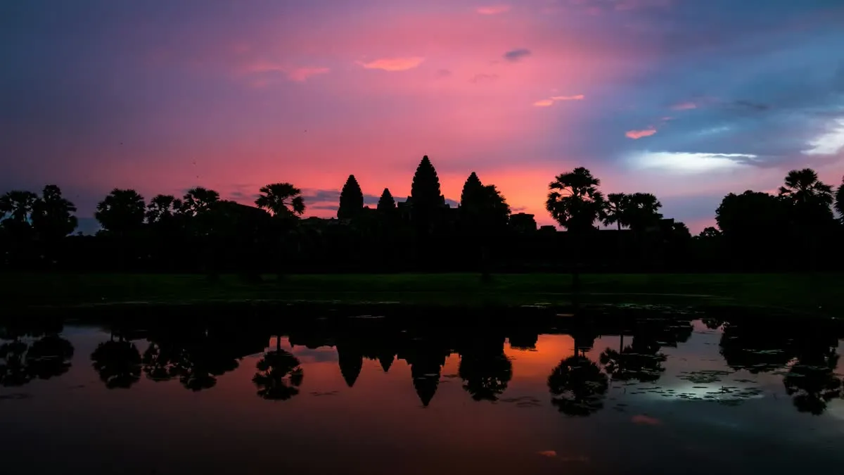 Stunning silhouette of Angkor Wat with a vibrant sunset reflecting in the surrounding water.