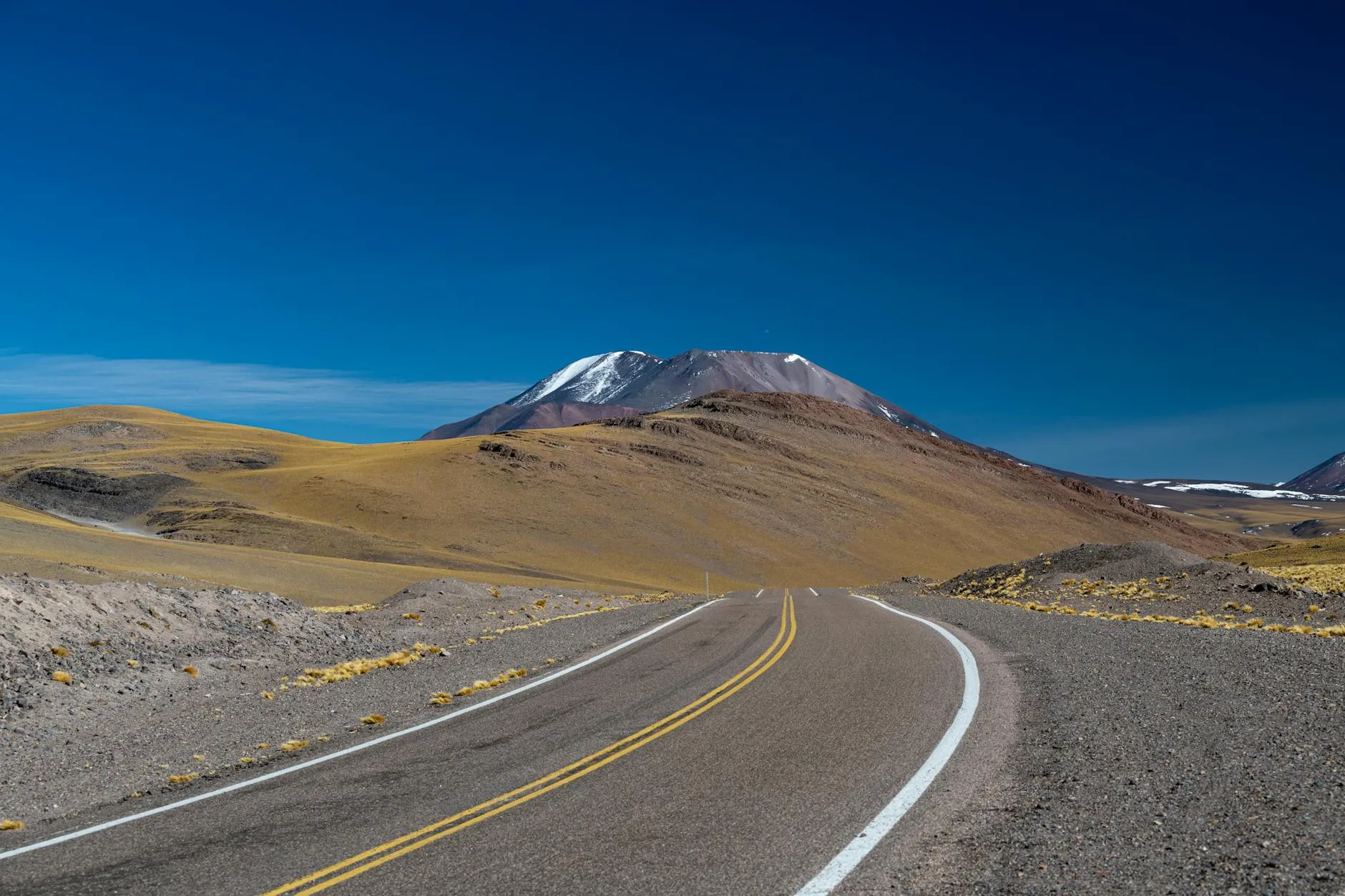 A winding road leading to a snow-capped mountain under a clear blue sky.