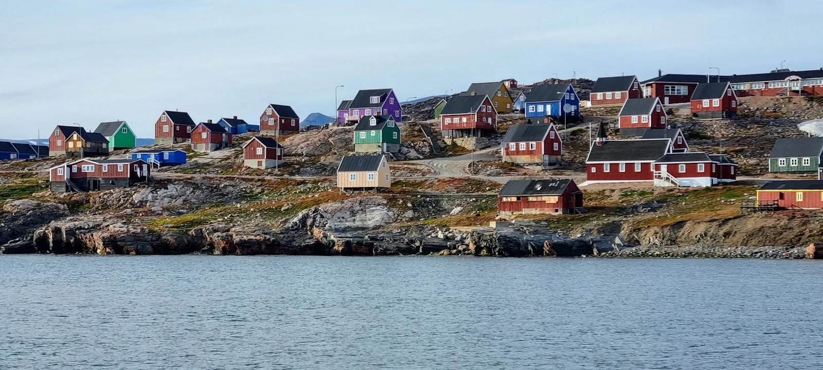 Colorful houses along the coast of a Greenlandic town with icebergs in the background