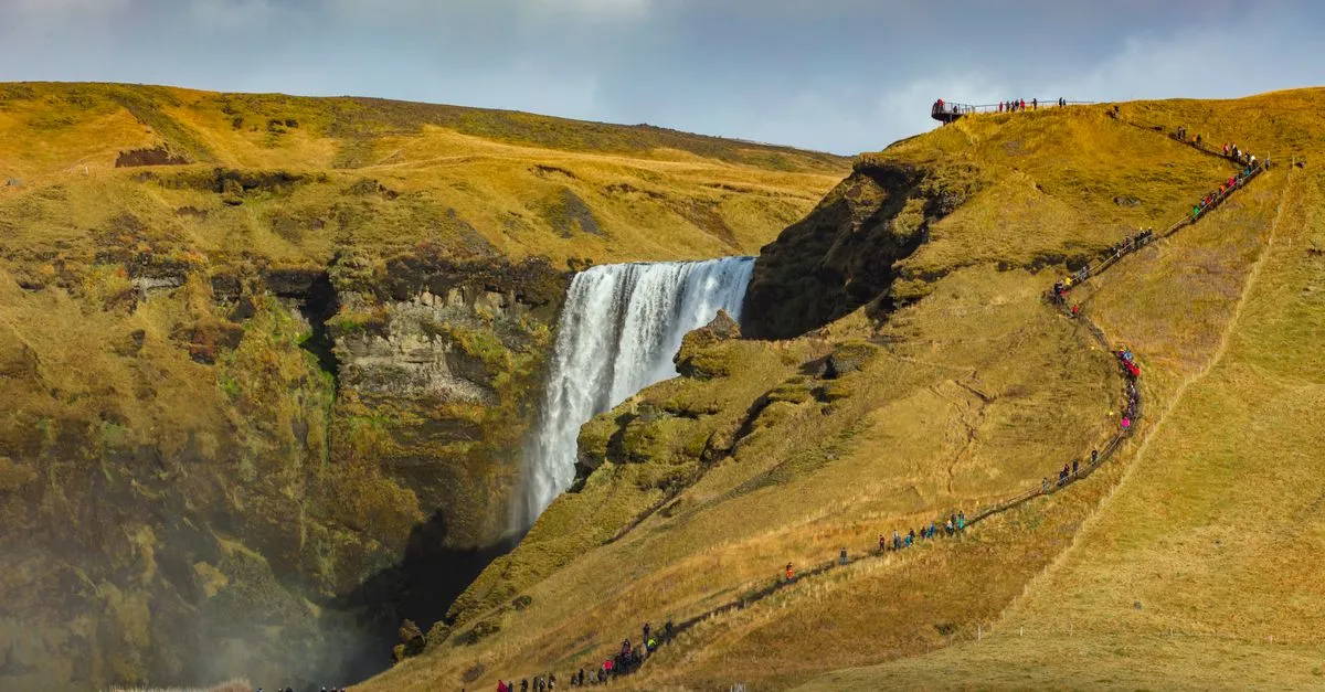 The broad curtain of Skógafoss waterfall with hikers at its base for scale