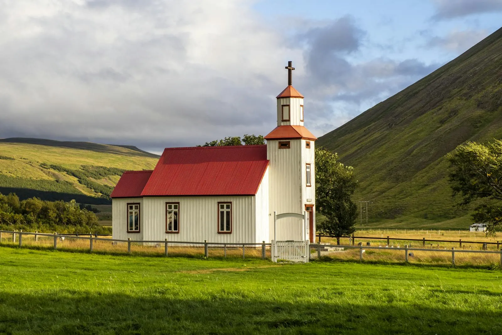 Small Icelandic church standing alone in a green countryside with mountains behind