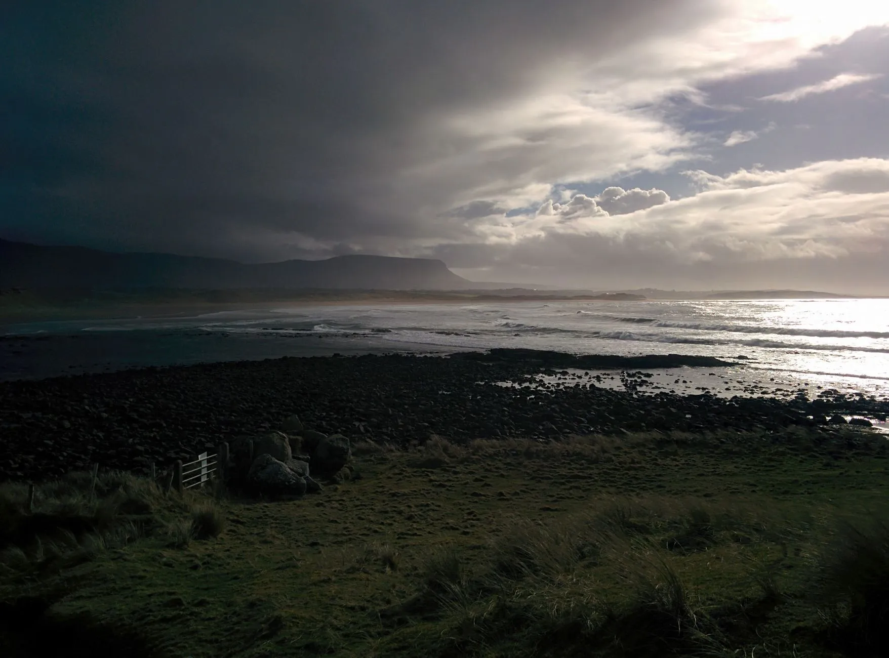 Lush green Irish landscape under dramatic sky with sunlight breaking through clouds