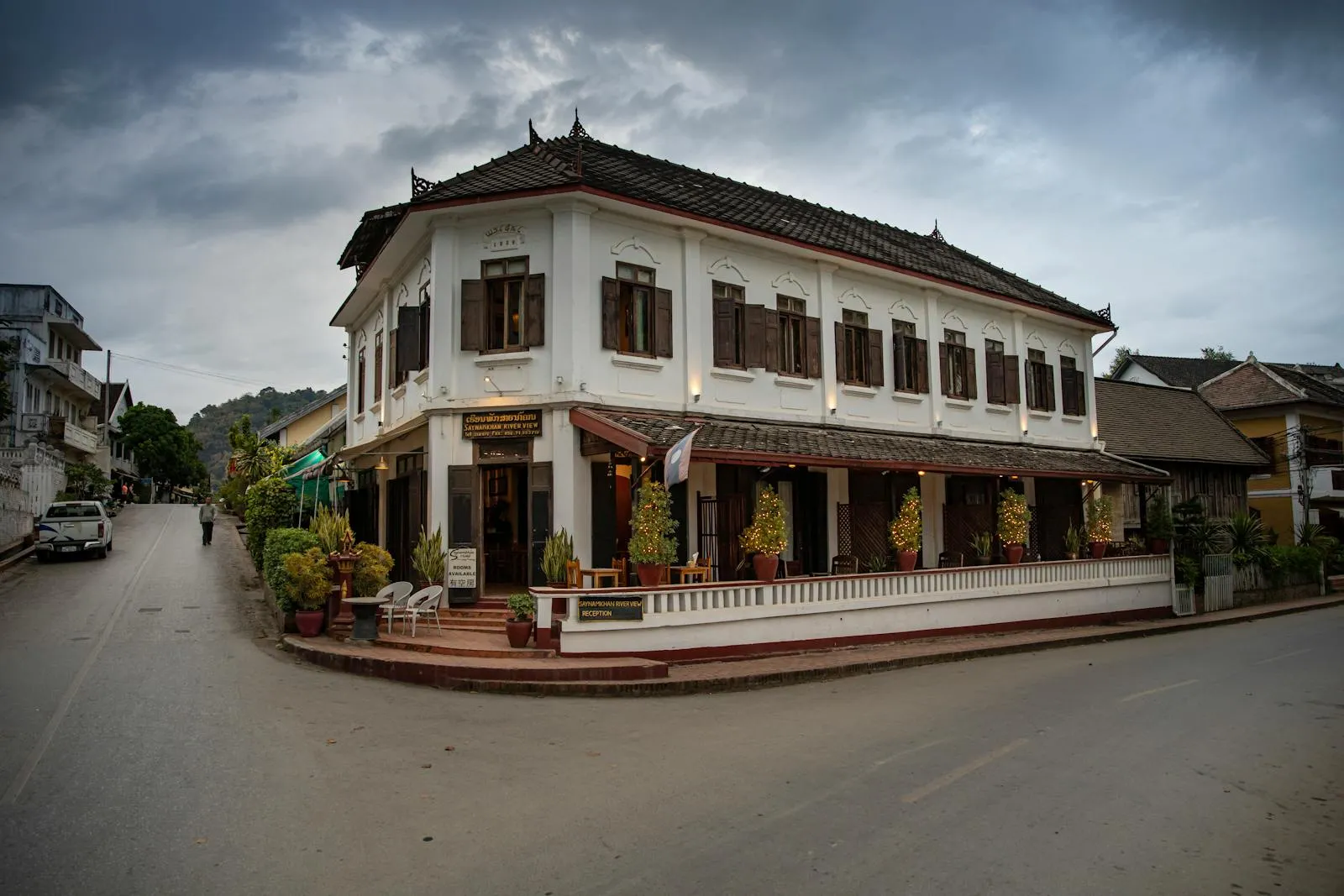 Elegant colonial-style building at a street corner in Luang Prabang, Laos, under cloudy skies.