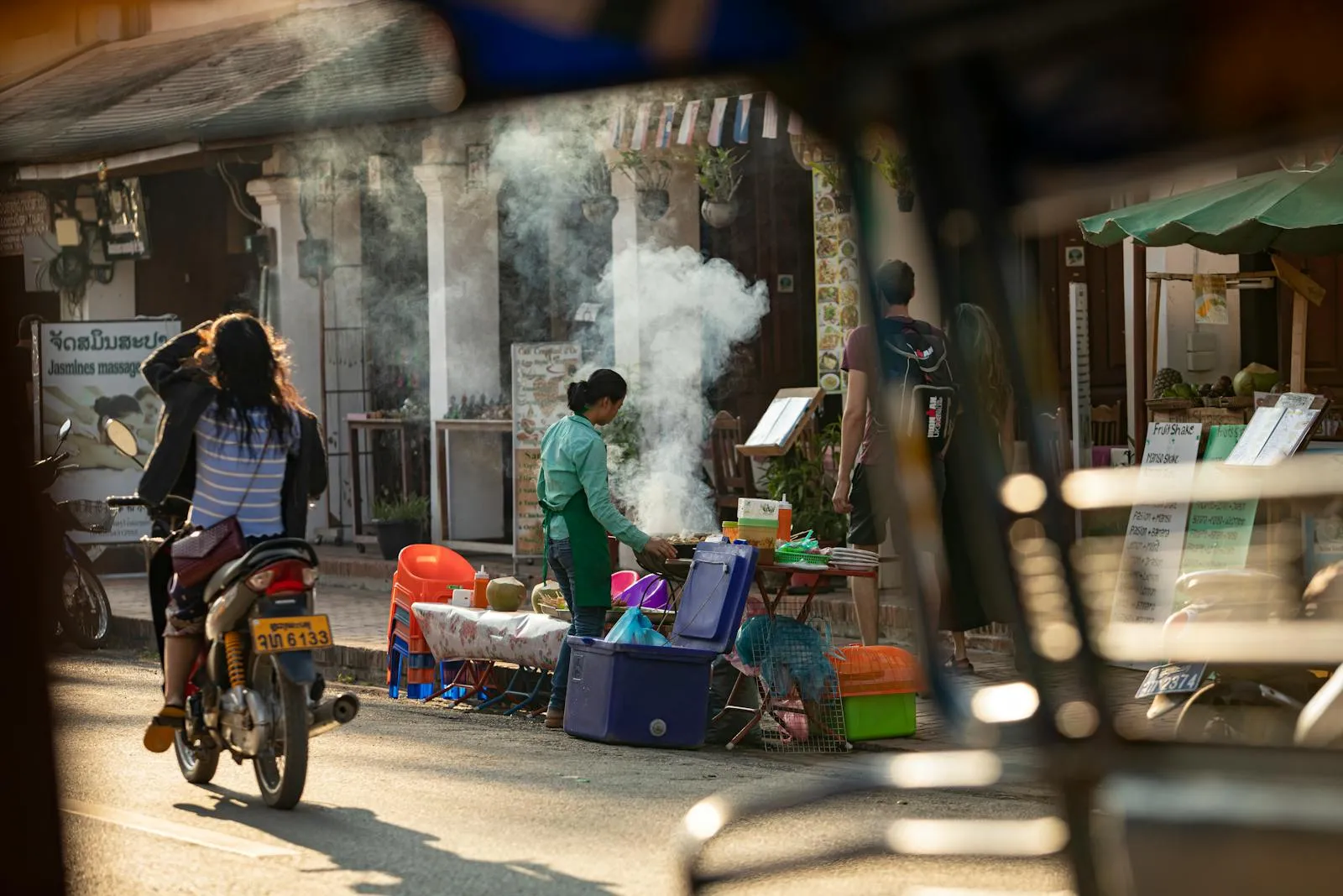 Street market with steaming food stalls and motorbike, capturing urban and cultural atmosphere.