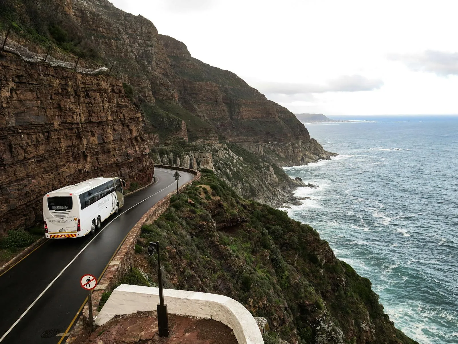 Yellow public bus winding along a coastal road with volcanic cliffs and ocean backdrop