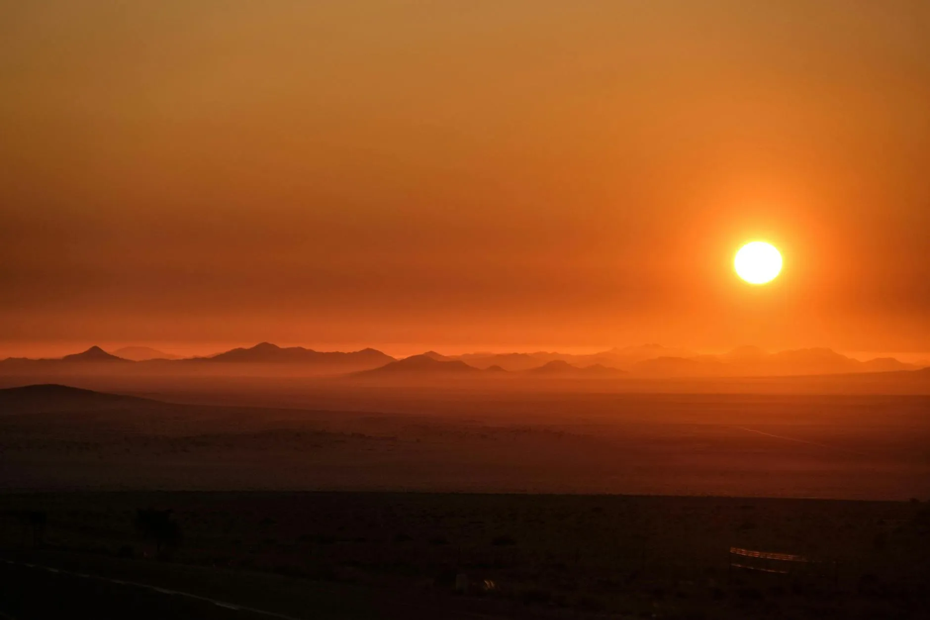 A stunning sunset casting vibrant orange hues over distant desert mountains.