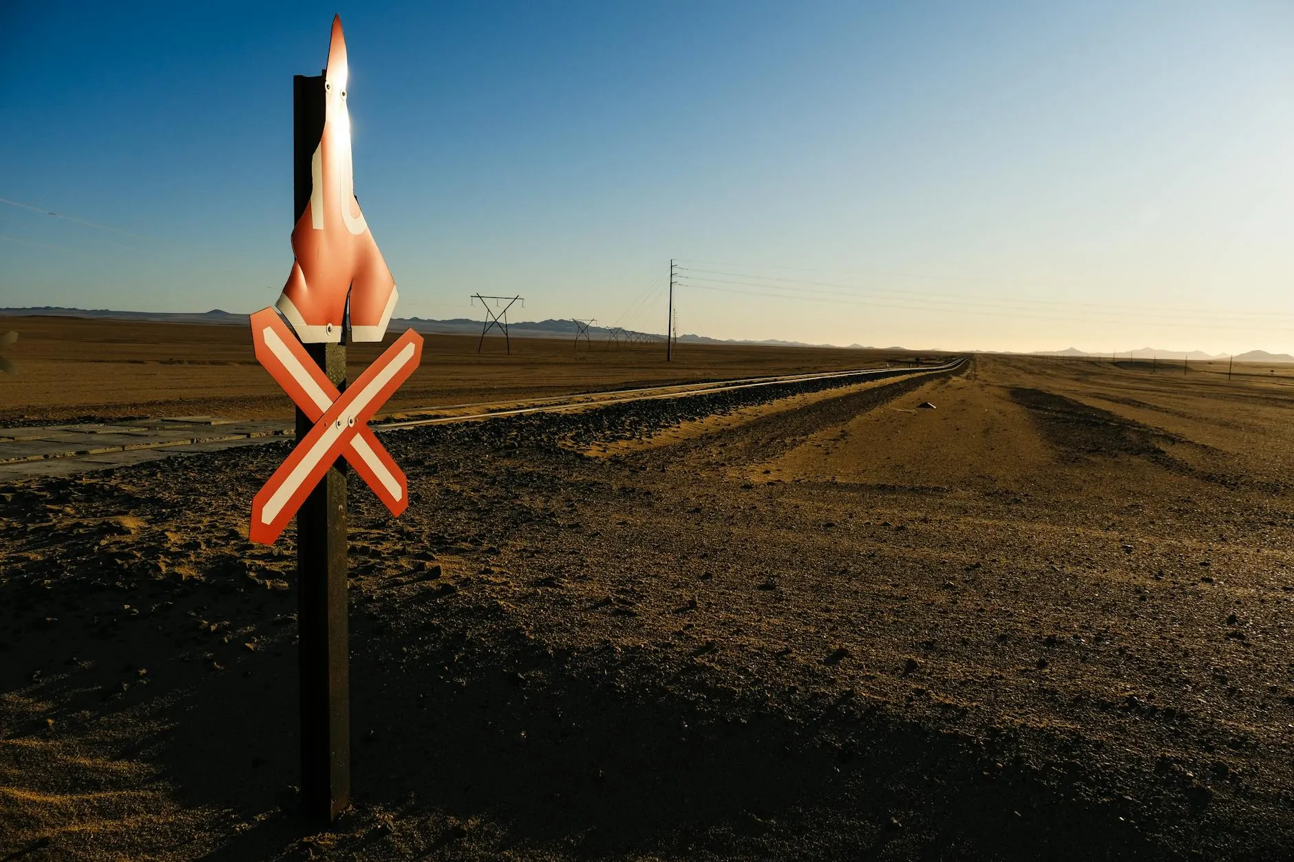 Empty desert railroad scene with a warning sign, clear sky, and distant mountains.