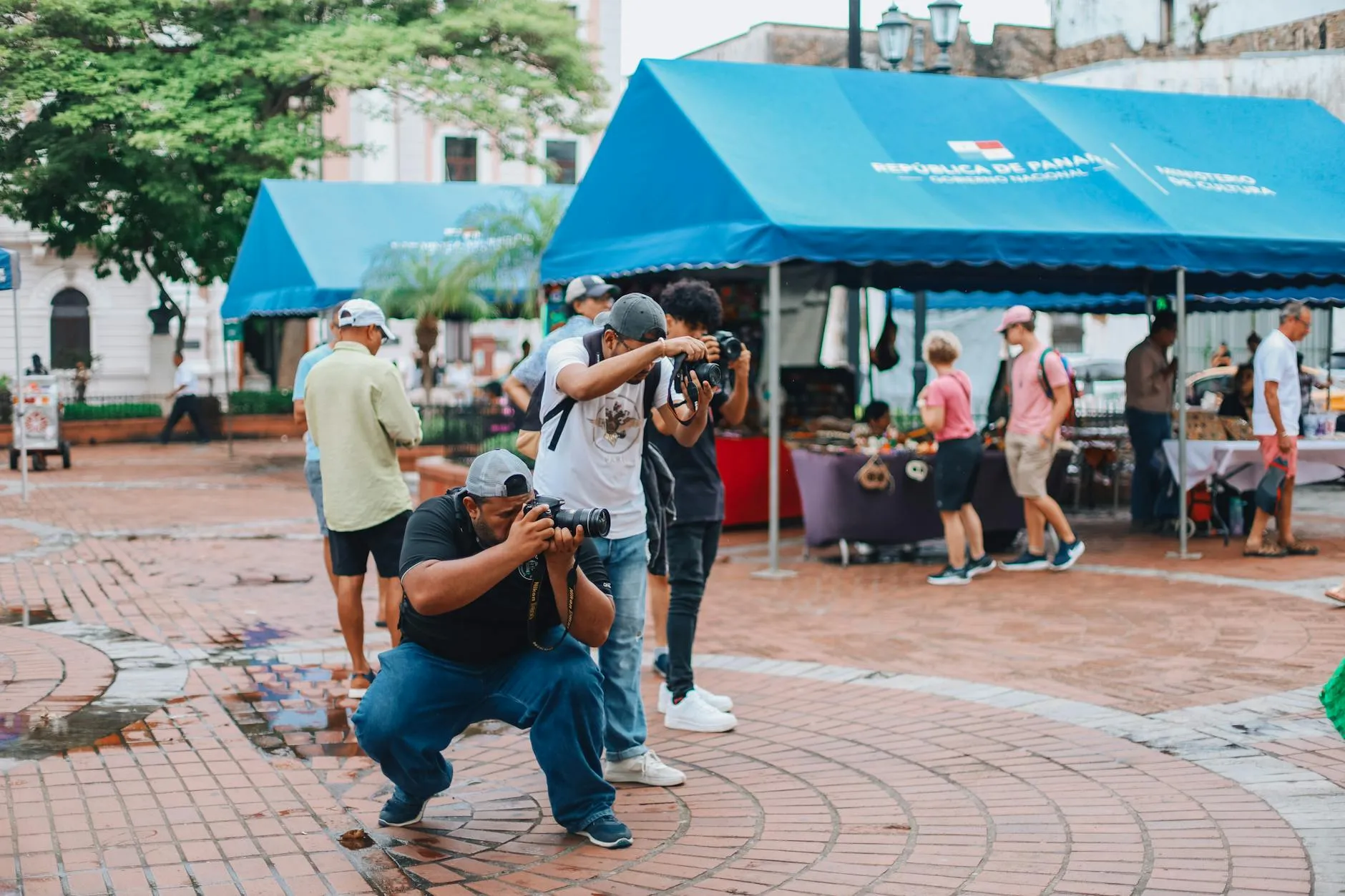 Photographers capturing moments in an urban Panama park with market stalls and diverse people.