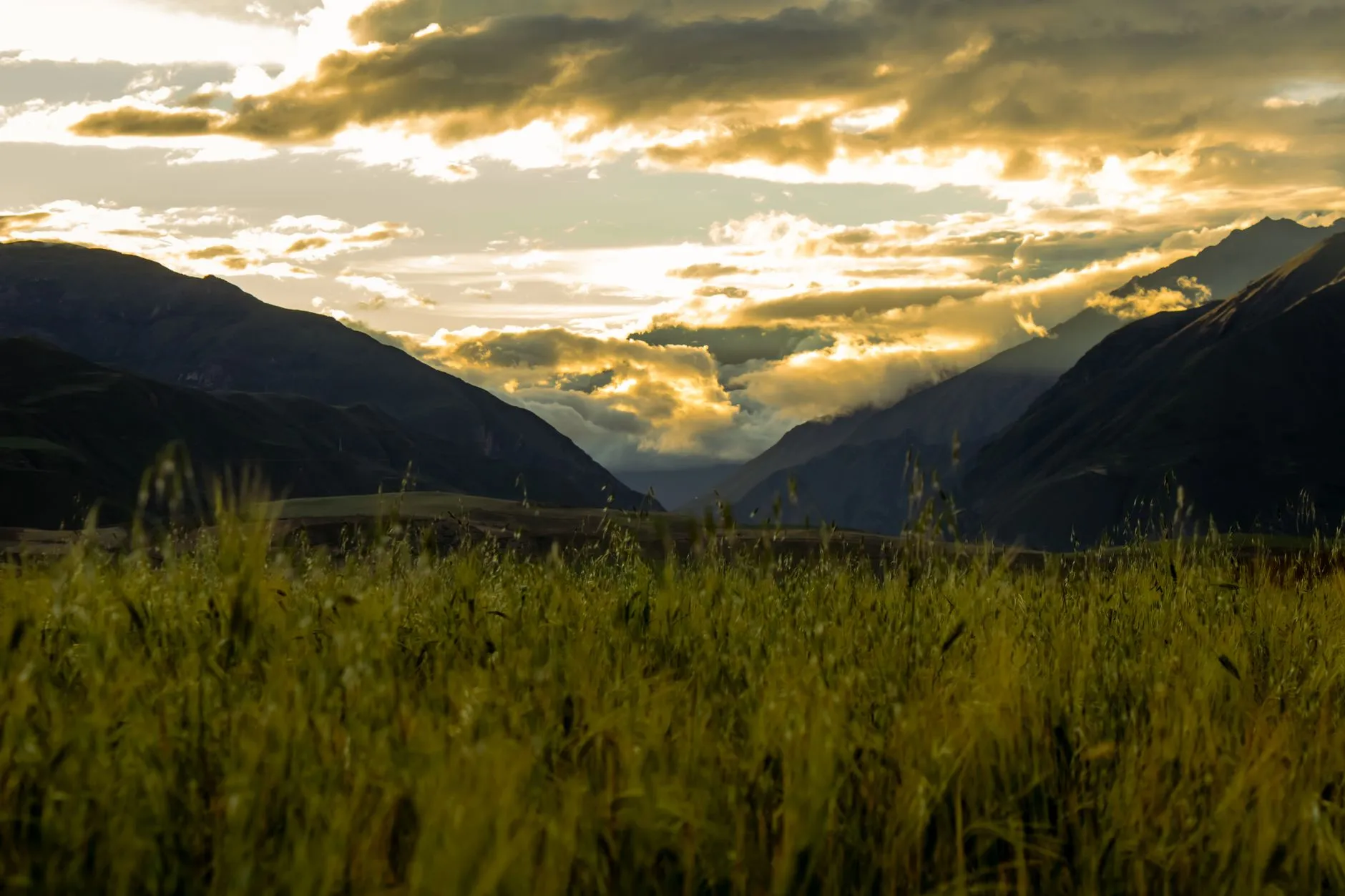 Stunning sunset view of the Andean mountains and fields in Cusco, Peru, highlighting serene nature and dramatic clouds.