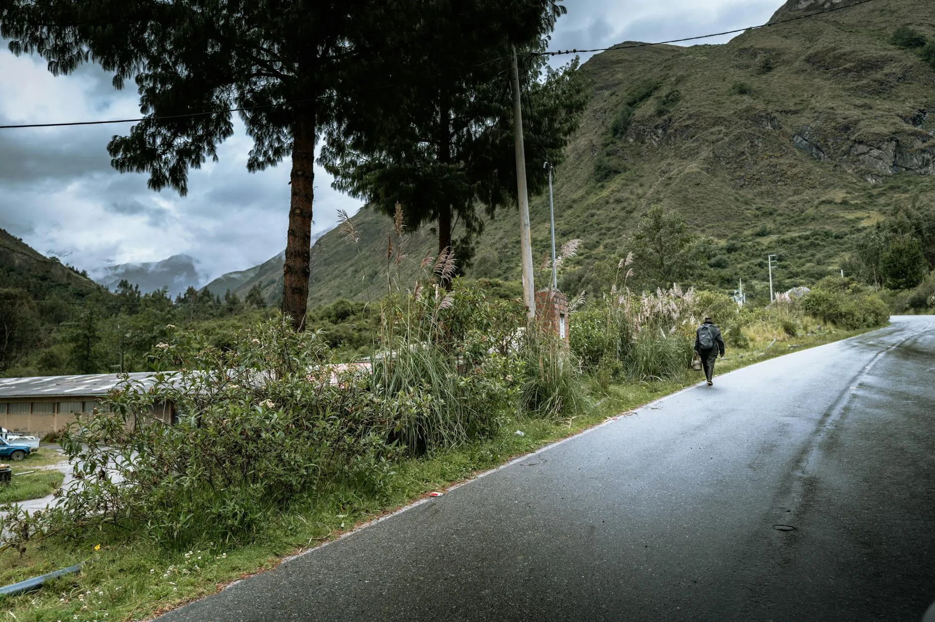 Lone traveler walking along a scenic mountain road in Huaraz, Peru under cloudy skies.