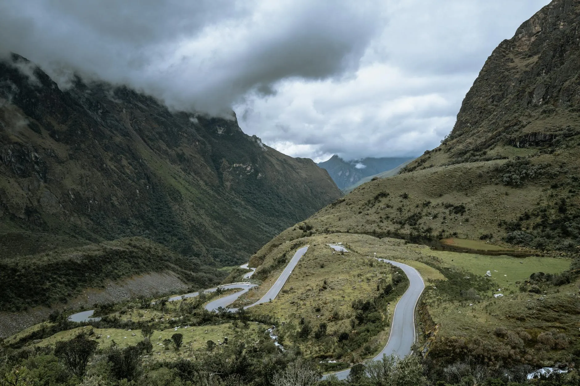 Serene winding road through the lush Peruvian Andes with dramatic clouds above.