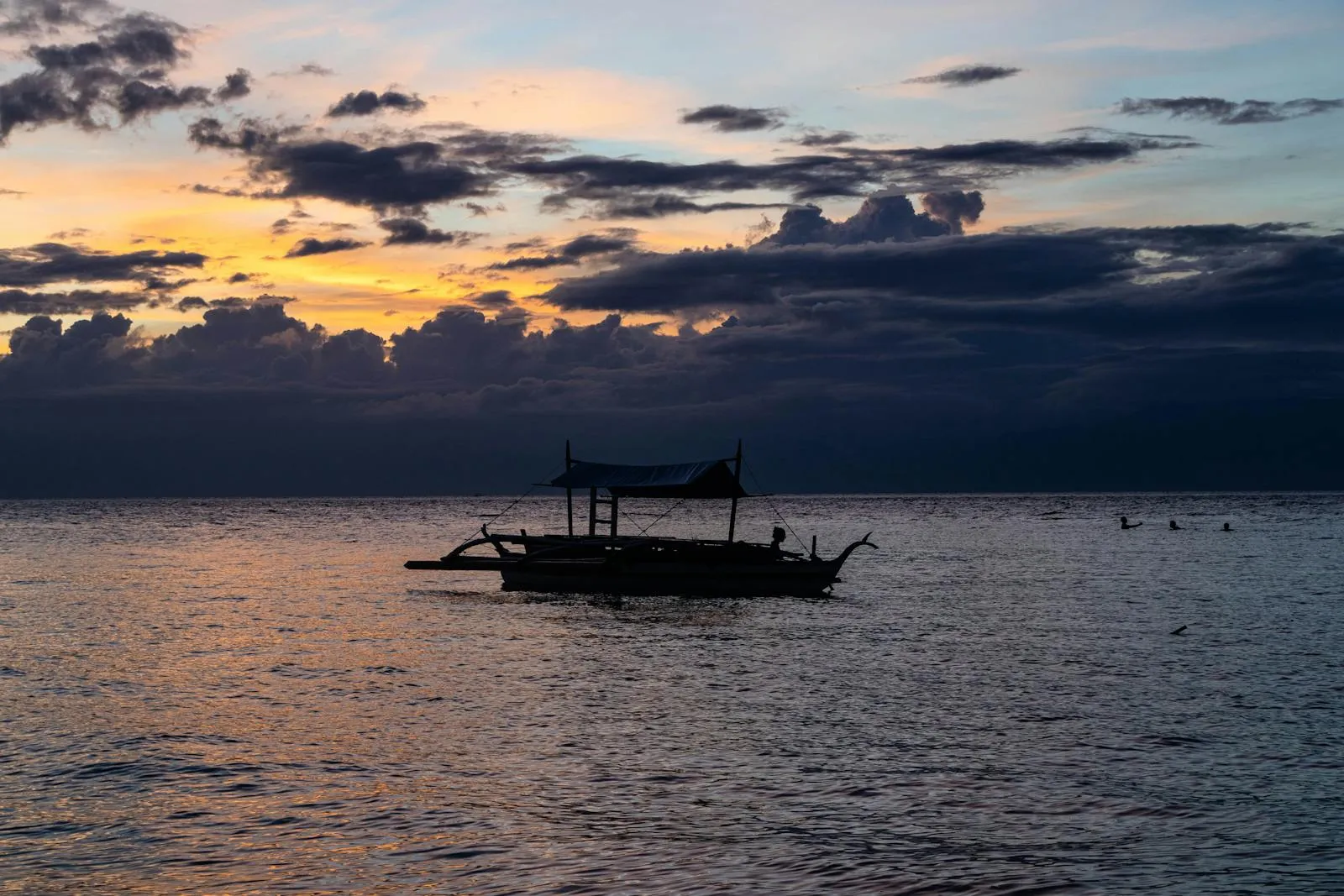 Serene sunset view with a silhouette of a traditional boat on the waters of Moalboal, Philippines.