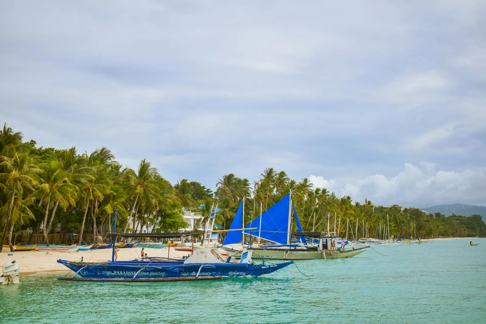 Serene tropical beach with blue sailboats and coconut trees in Boracay, Philippines.
