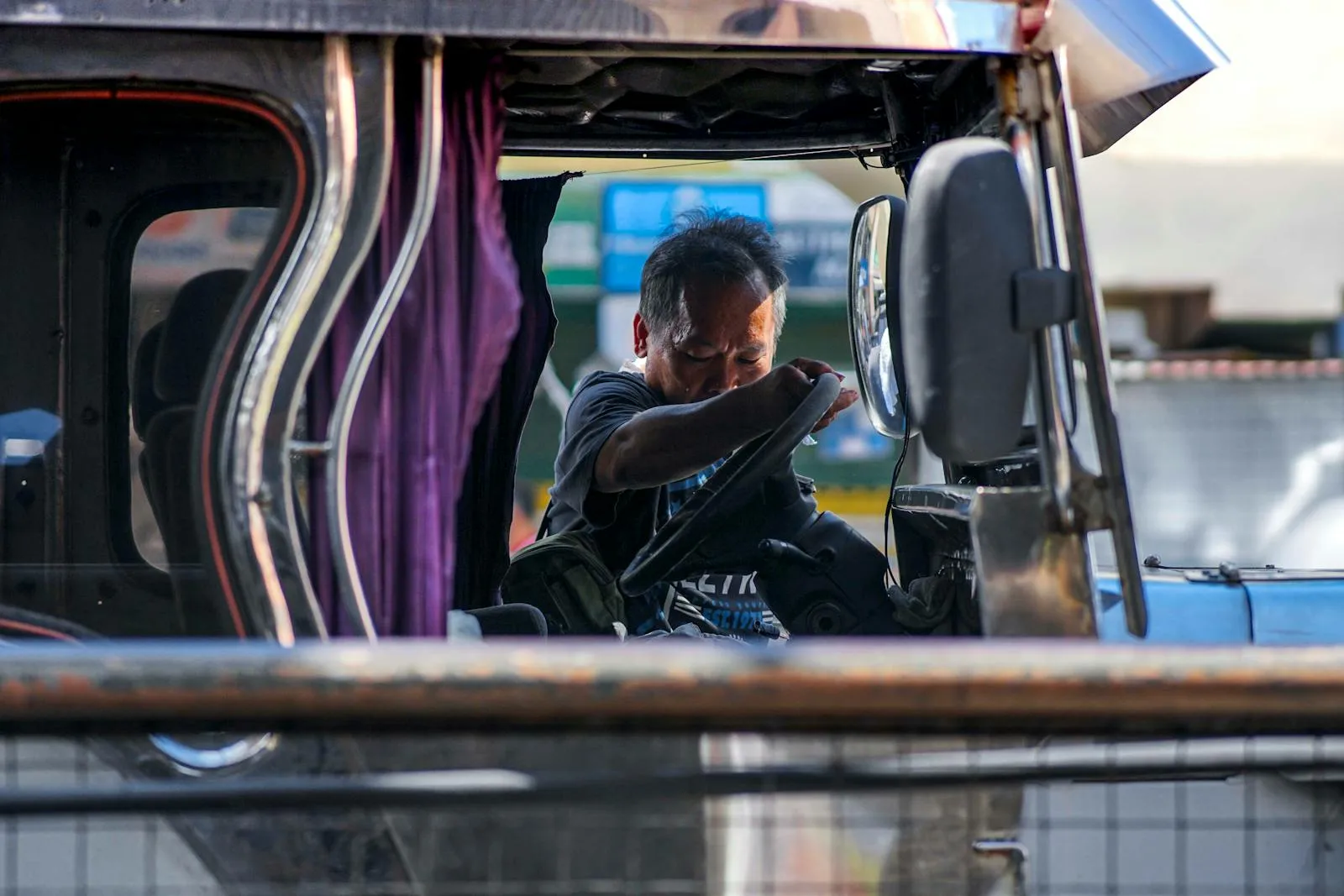 A jeepney driver napping inside his vehicle in Manila, Philippines. Daytime scene capturing urban life.