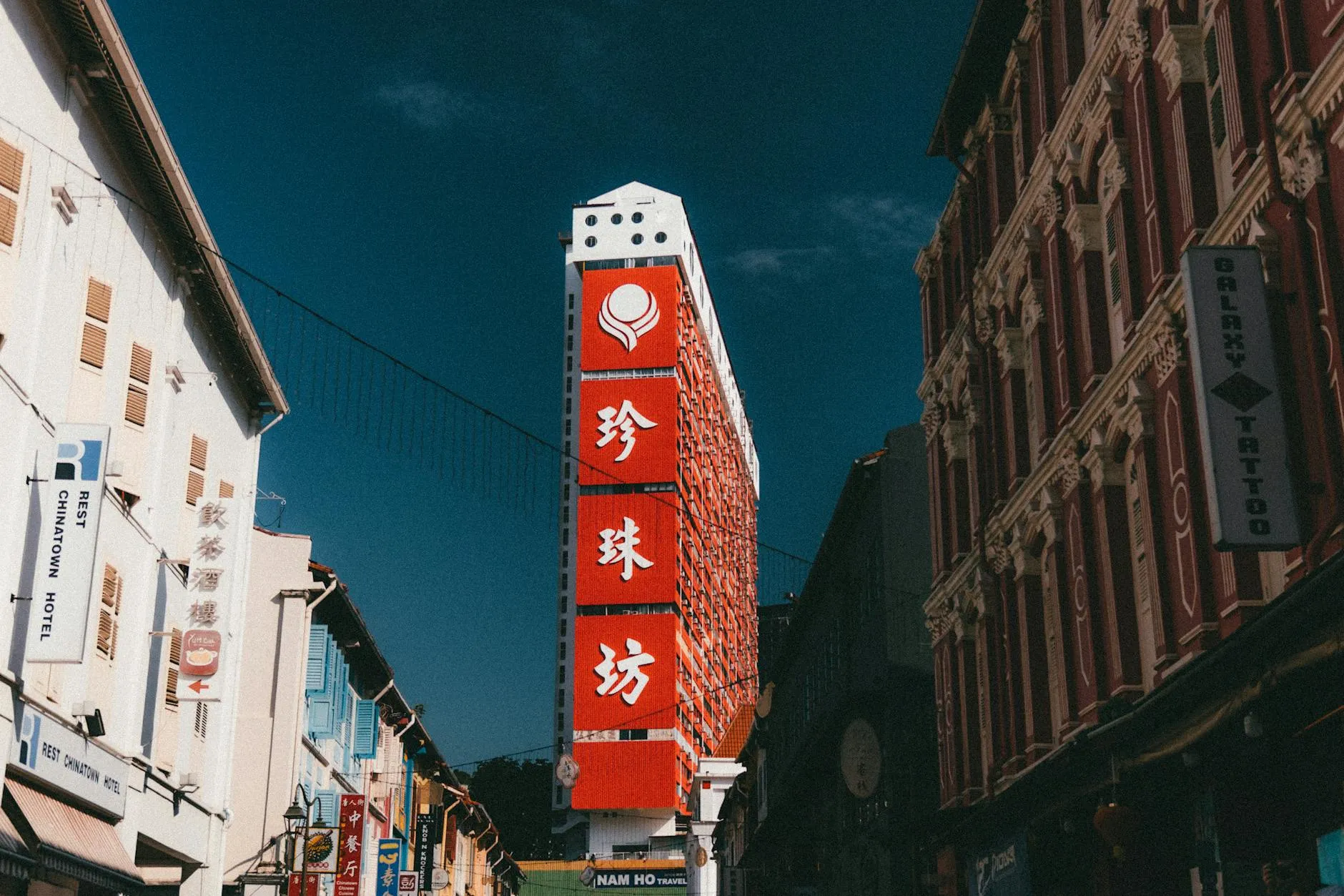 Vibrant Chinatown street in Singapore featuring a tall, iconic red building and busy storefronts.
