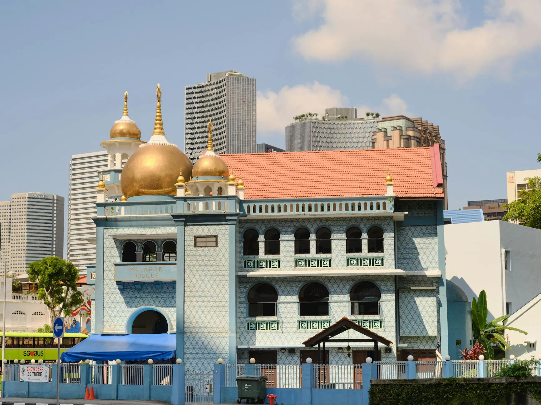 Masjid Sultan facade with golden domes and city skyscrapers behind on a sunny day.