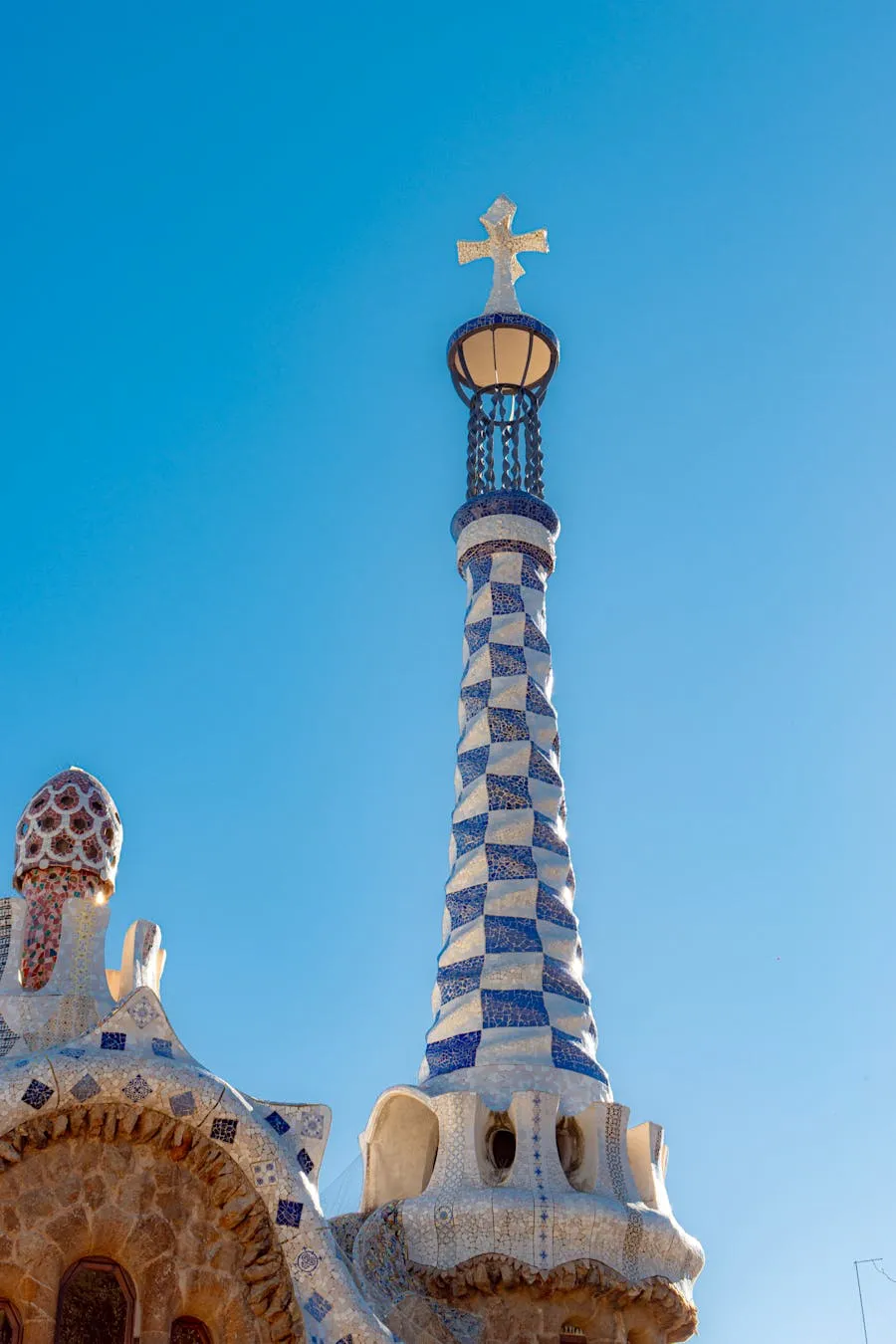 Mosaic-covered spire and rooftops in Park Guell with Barcelona skyline beyond