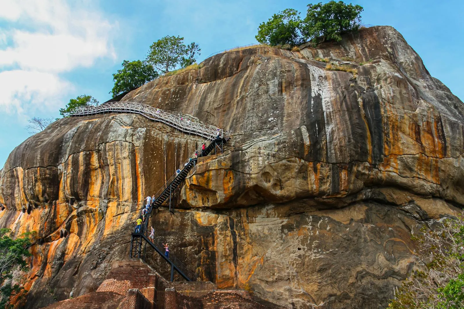 A breathtaking view of Sigiriya Rock Fortress, a UNESCO World Heritage site in Sri Lanka, with stairs and tourists ascending.