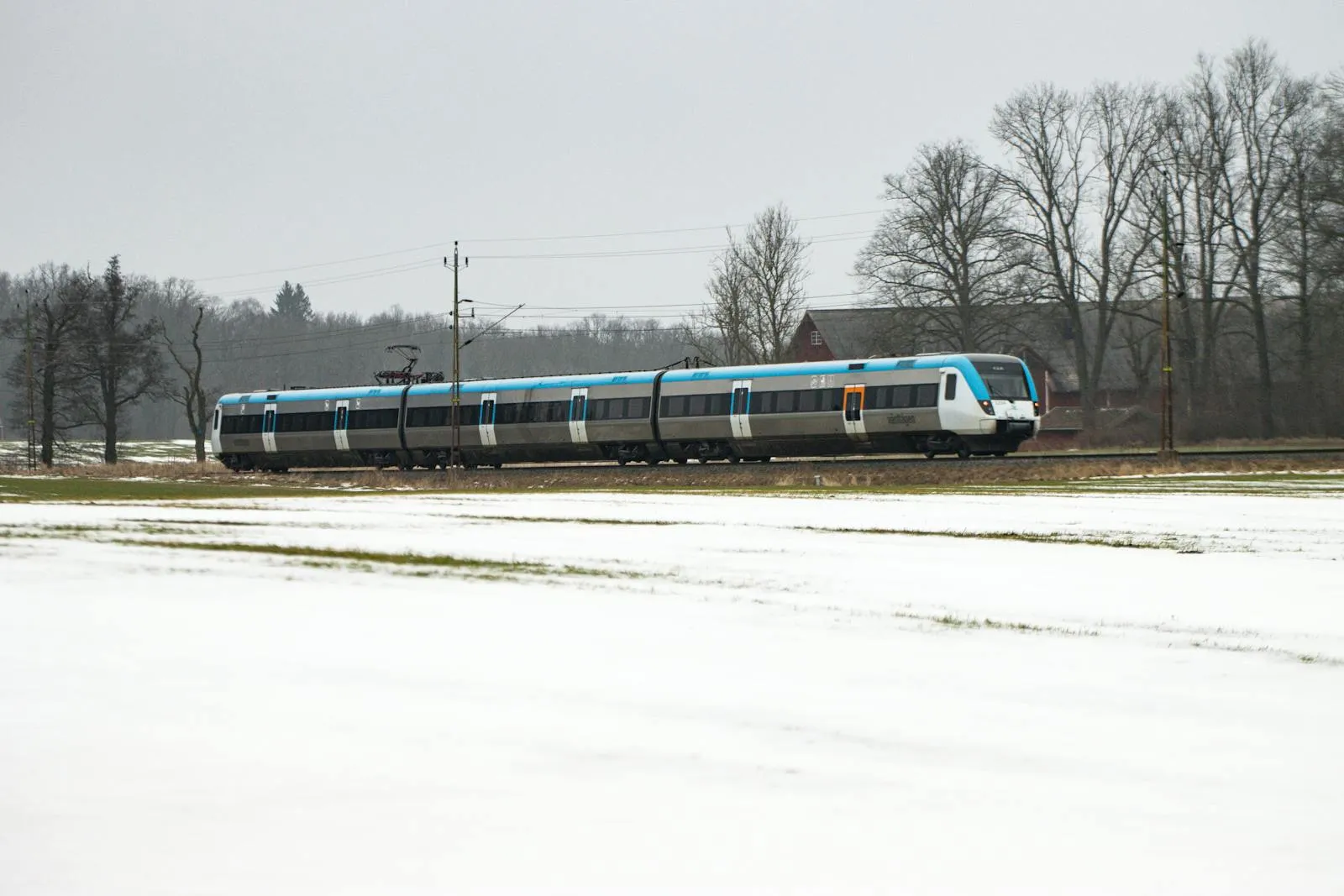 Swedish train passing through green countryside with red houses in the distance