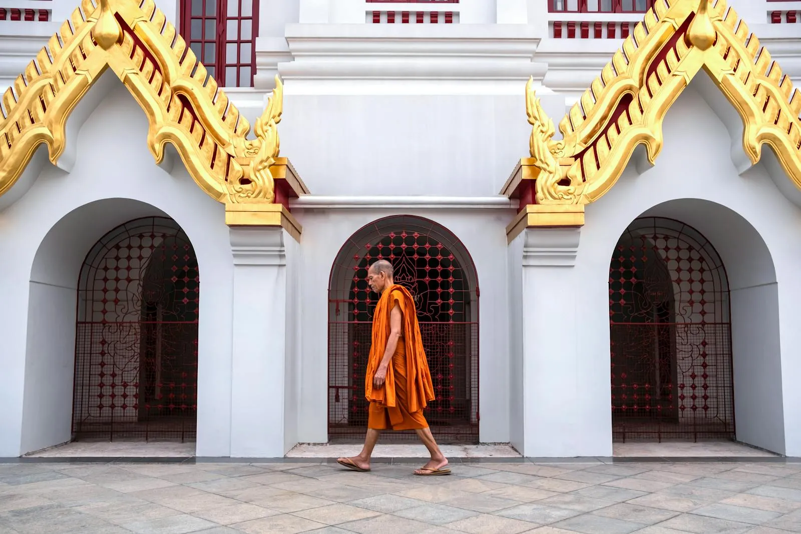 A Buddhist monk walks past the ornate architecture of Loha Prasat Temple in Bangkok, Thailand.