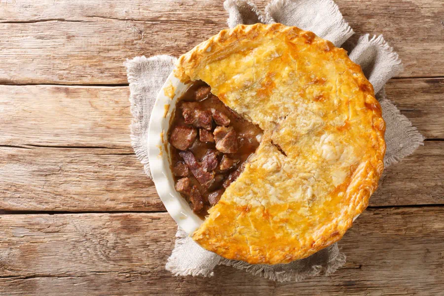 Steak and ale pie with golden pastry crust on a pub table