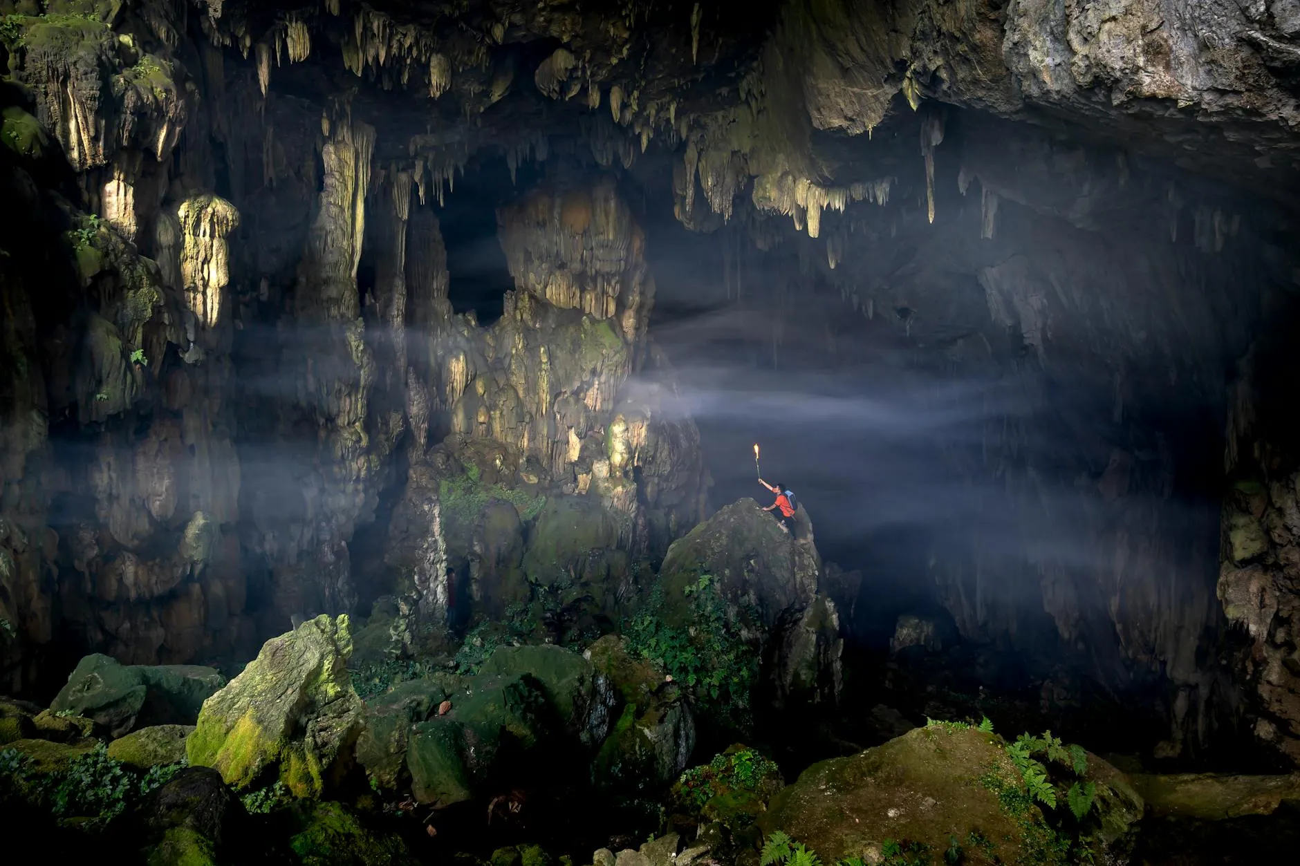 A lone explorer illuminates a vast, mysterious cave in Son La, Vietnam with a torch, showcasing nature's hidden wonders.